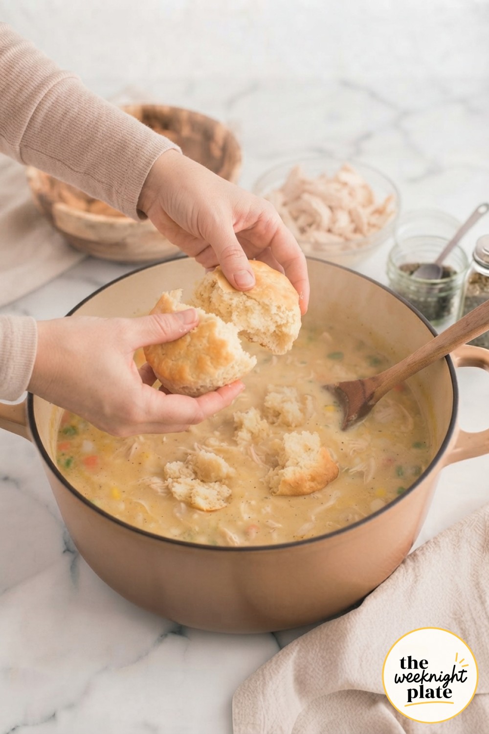 Tearing a baked golden biscuit by hand and dropping it into thick, creamy chicken pot pie soup