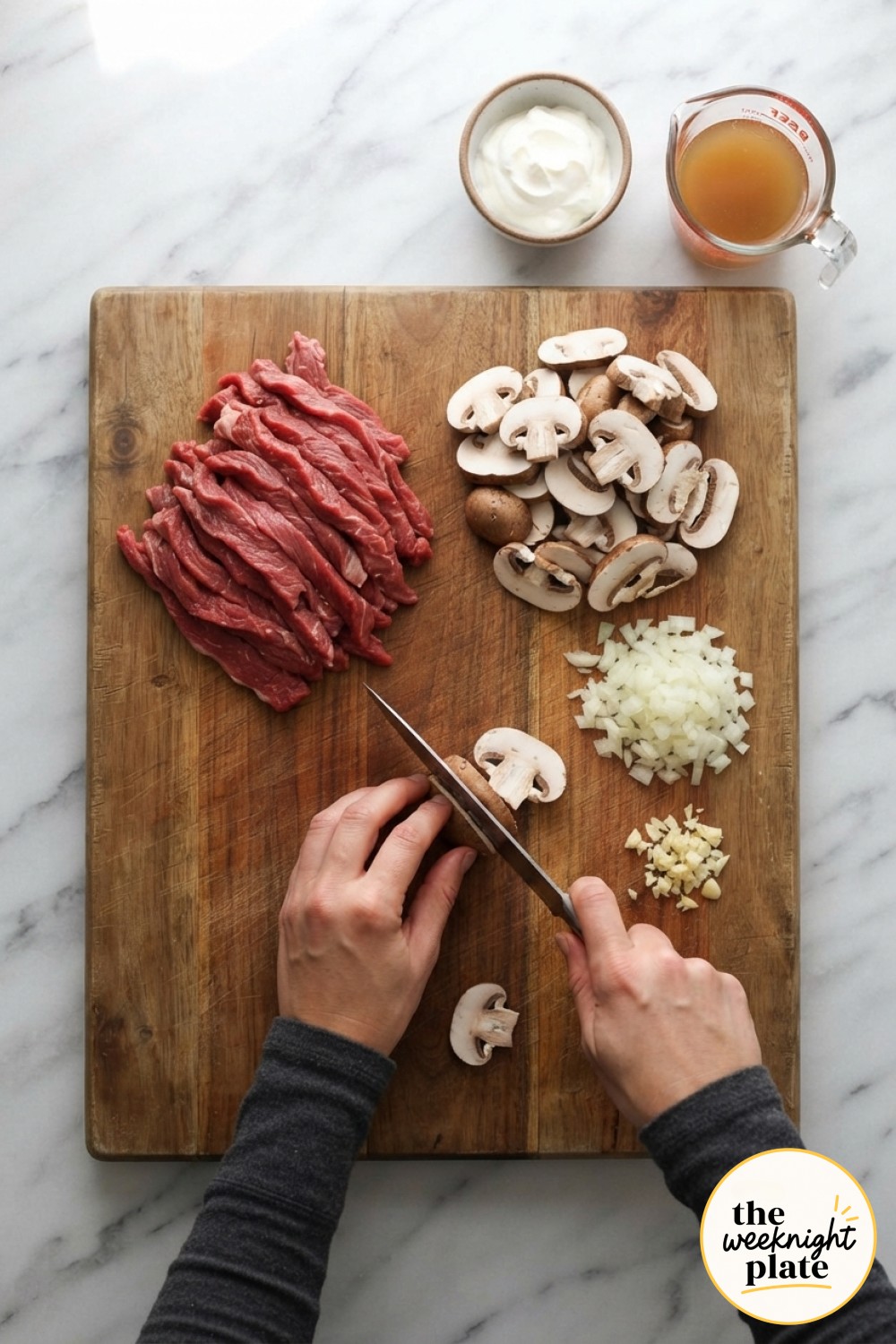Raw beef strips, sliced mushrooms, onion and garlic arranged for low carb beef stroganoff prep on a board.