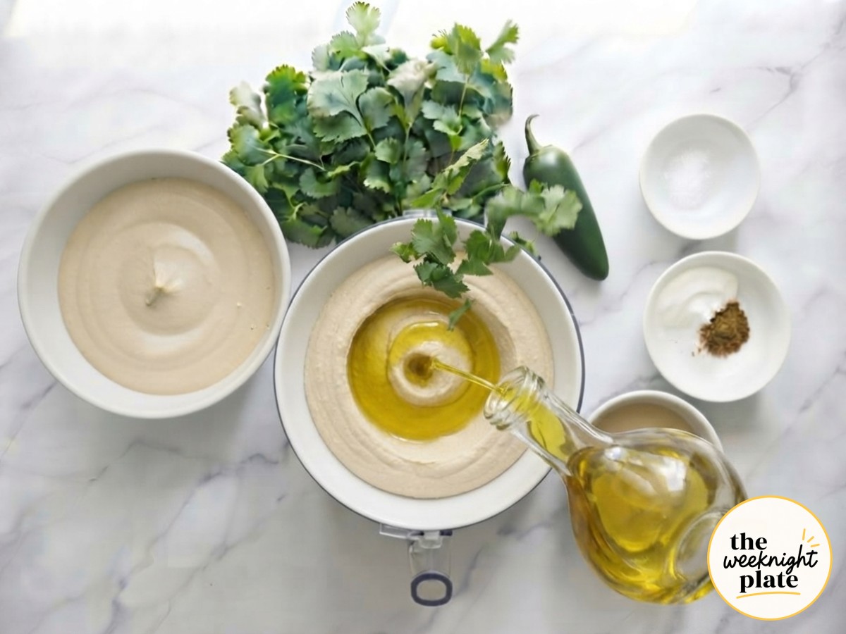 Golden olive oil drizzling into a mediterranean hummus bowl with cumin nearby